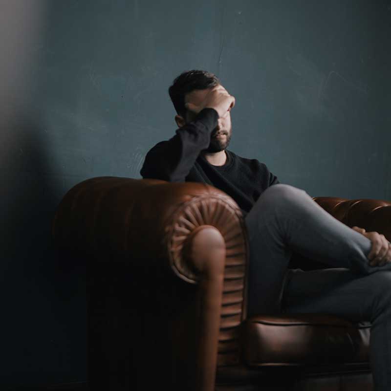 Young man covering his eyes, on a couch in a Mates Matter Counselling therapist's office